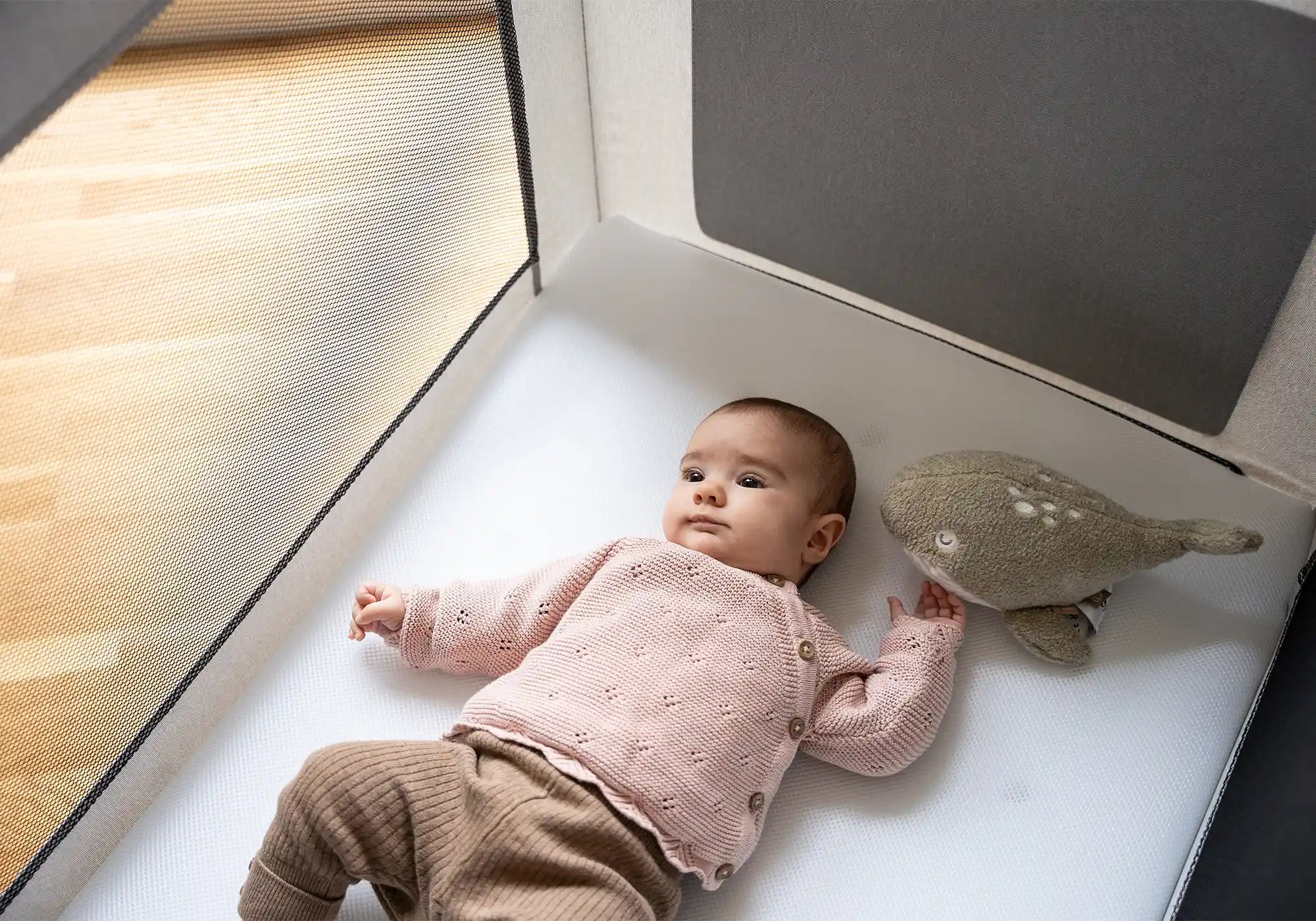 Baby mit Kuscheltier liegt im Kids Alm Fresh Air Reisebett