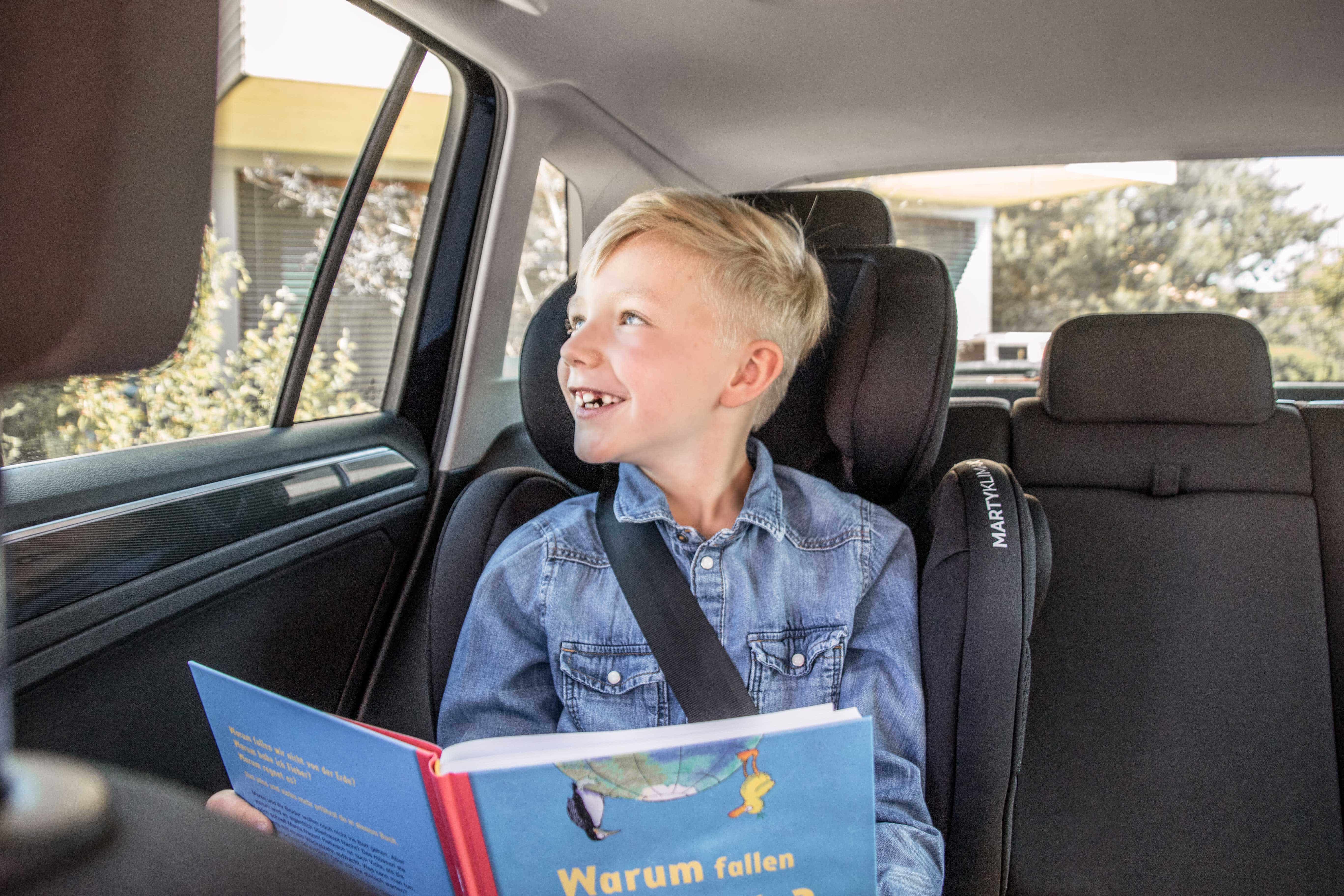Kind im Kindersitz im Auto mit Buch